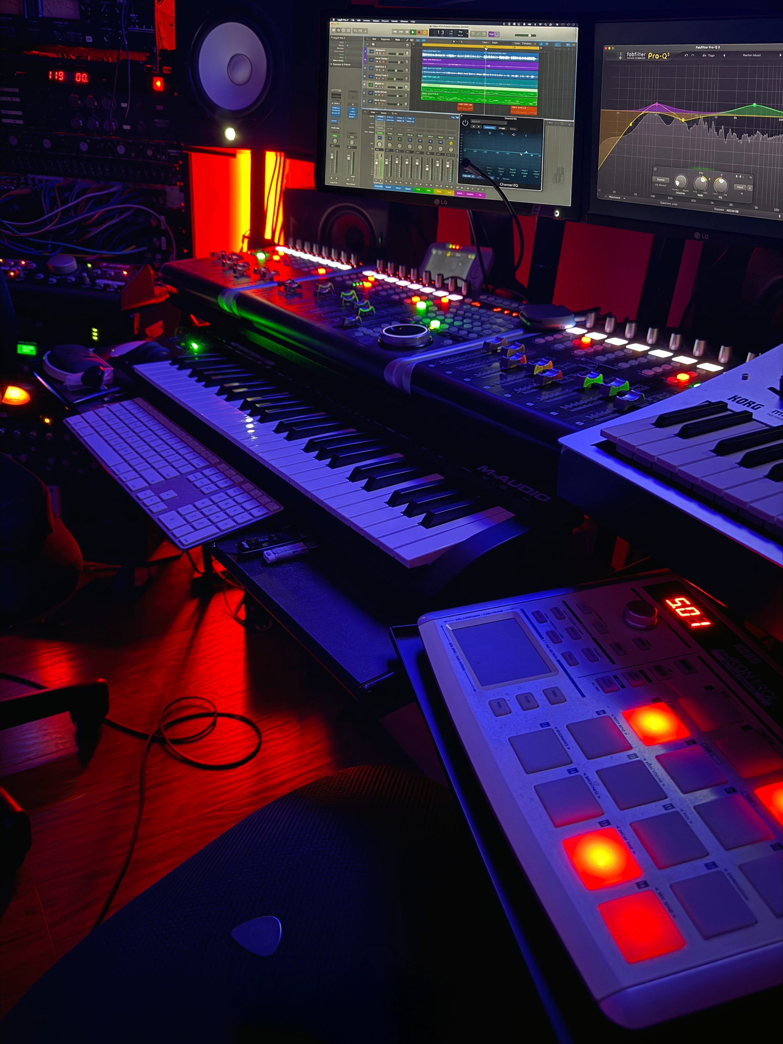 Music production studio with digital audio workstation on dual monitors, keyboard, MIDI controller, synthesizer, and studio monitors, illuminated by colorful LED lights.