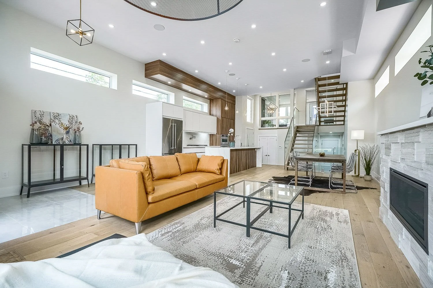 Striking open-concept living space with soaring ceilings, a sleek linear fireplace, floating staircase, and seamless flow into the contemporary kitchen and dining area