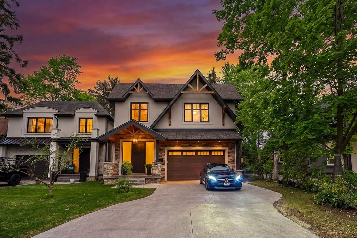 Luxury custom home exterior at twilight with illuminated windows, modern architecture and dramatic sunset sky