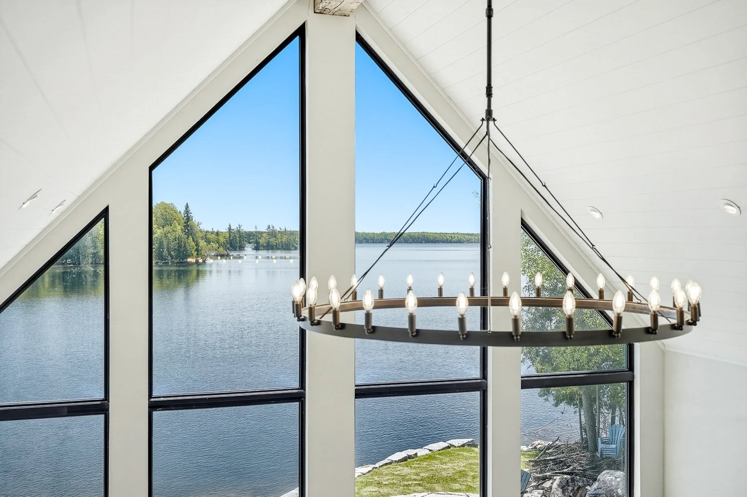 Panoramic waterfront view framed by soaring floor-to-ceiling windows, filling the home with natural light and showcasing the property's exceptional lakeside setting.