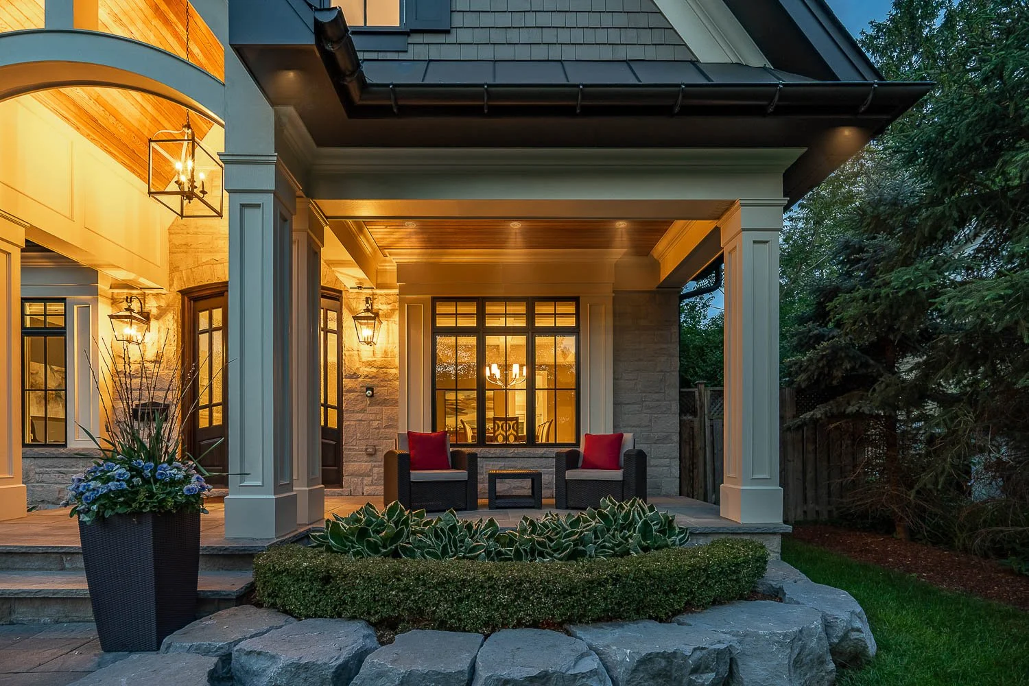 Luxury home front porch at twilight with stone exterior, covered seating area and warm lighting