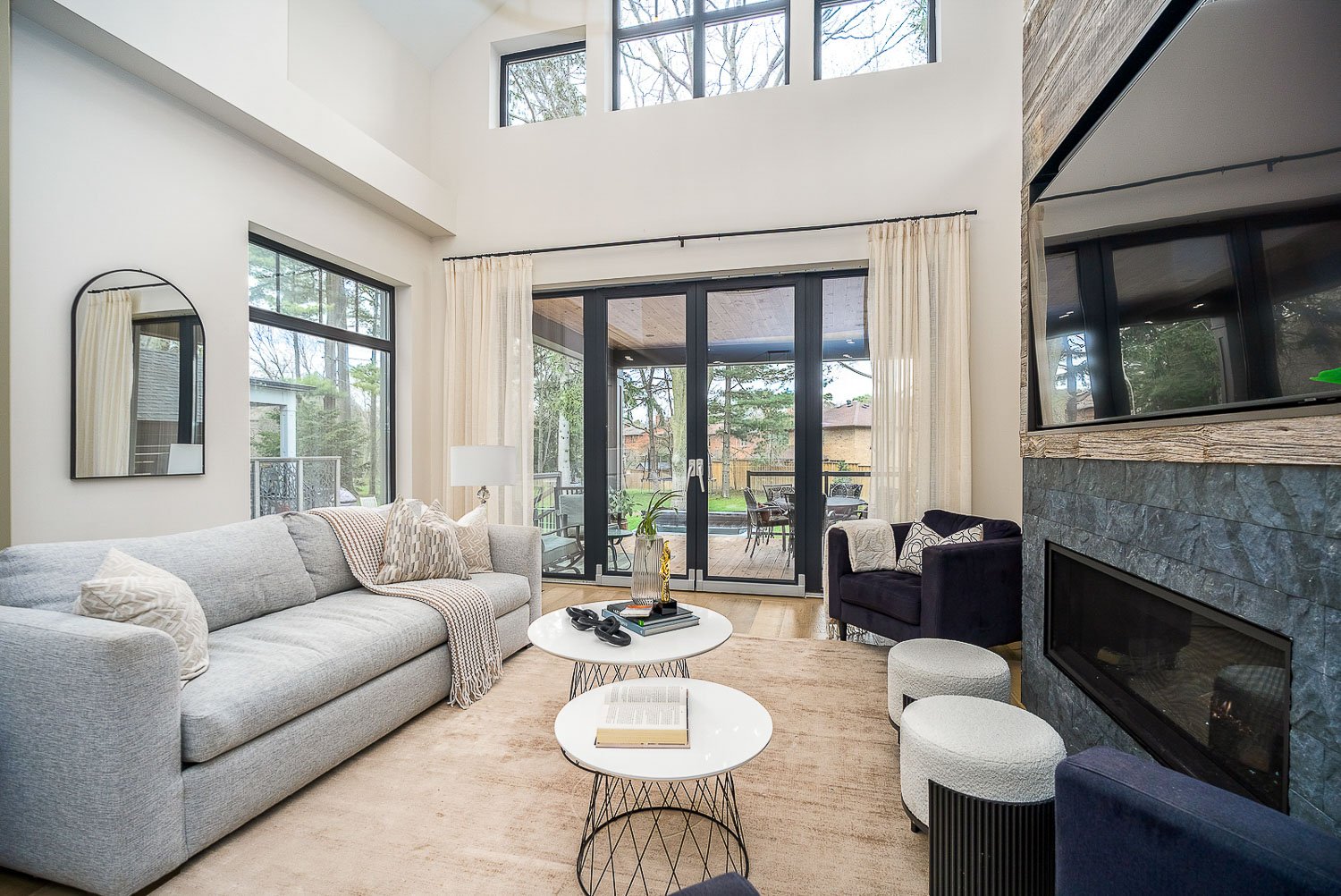Airy great room with soaring ceilings, expansive windows, and a sleek fireplace, seamlessly connecting the indoor living space to the covered outdoor entertaining area.