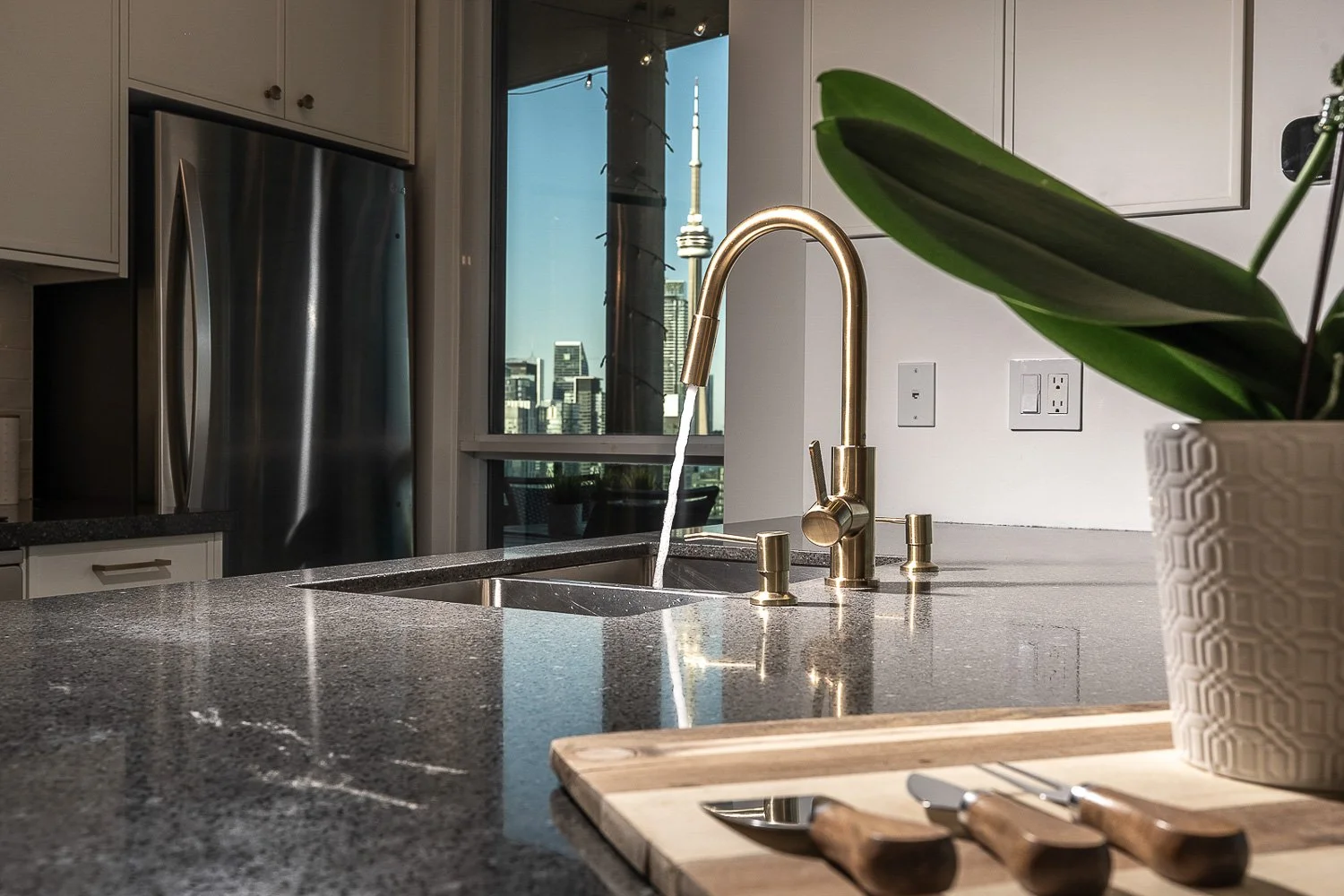 Modern kitchen with quartz island, brushed gold faucet and CN Tower city view