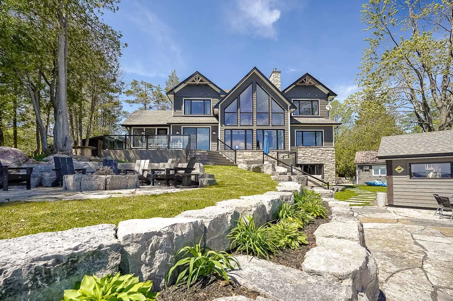 Stunning waterfront home with striking contemporary architecture, expansive lake-facing windows, tiered stone landscaping, multiple outdoor living spaces, and breathtaking shoreline views.