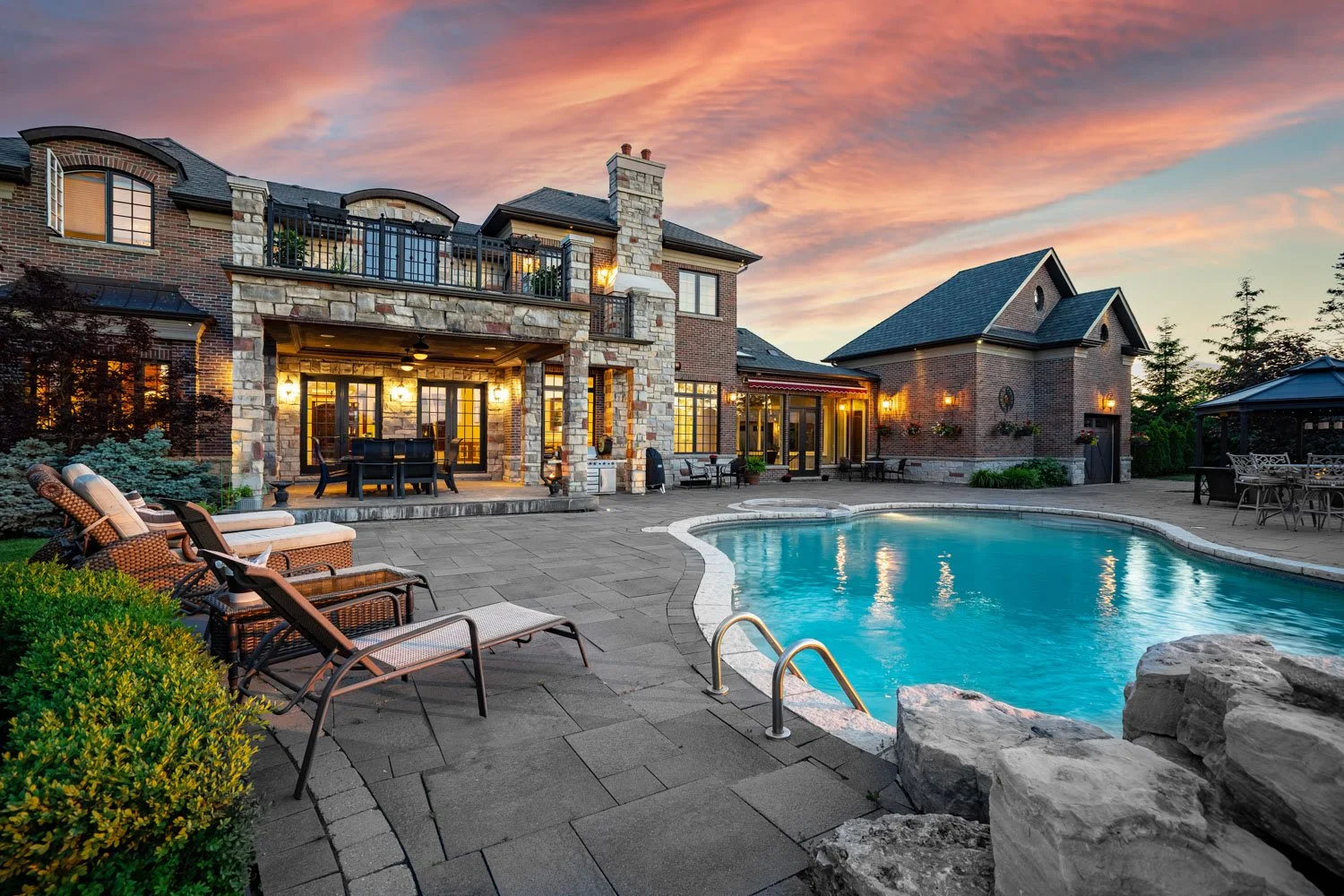 Luxury backyard with in-ground pool, stone patio and twilight sky behind an upscale home