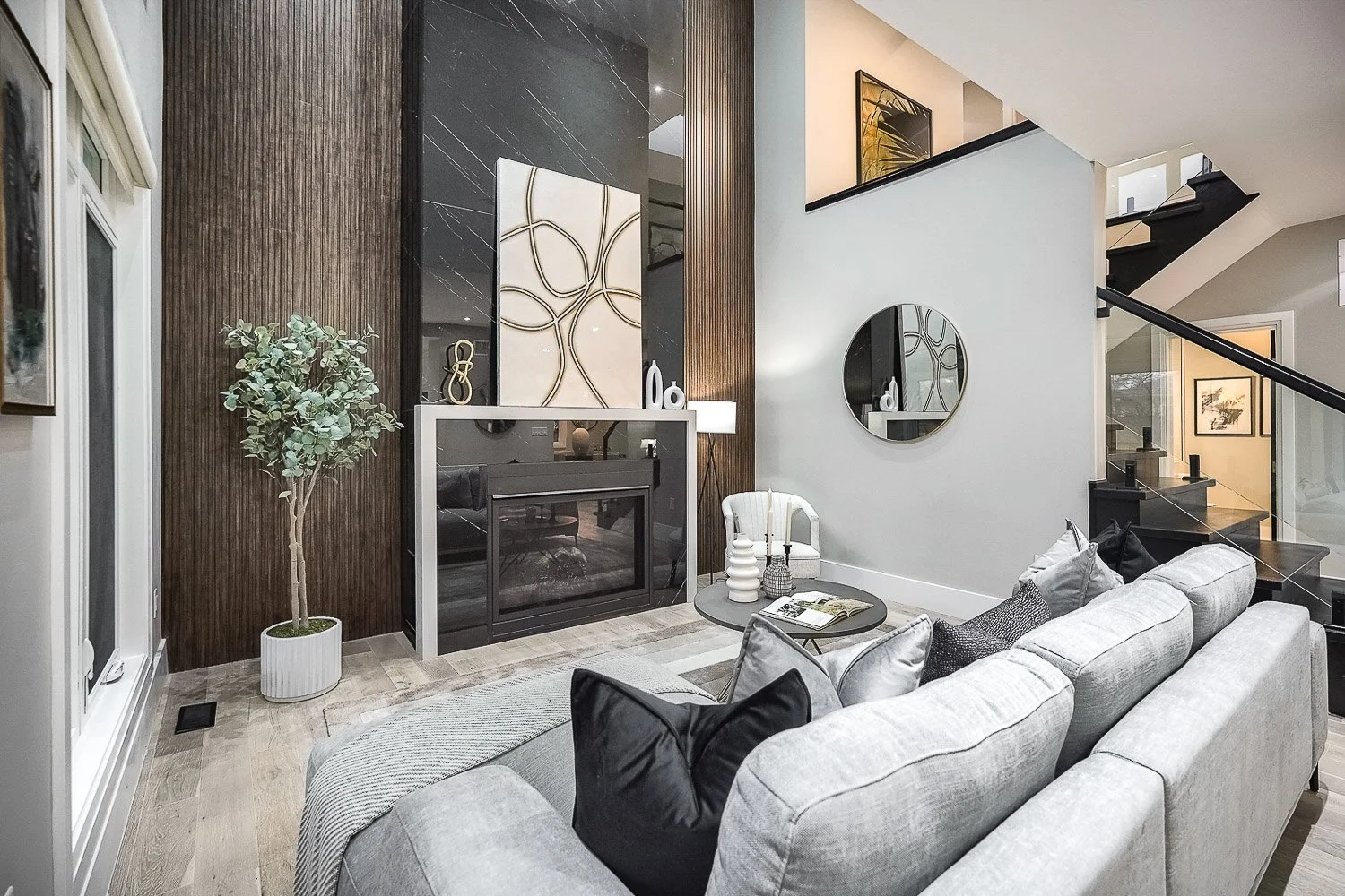 Contemporary living room with a dramatic floor-to-ceiling feature fireplace, rich wood accent wall, and modern floating staircase, creating a sophisticated architectural focal point.