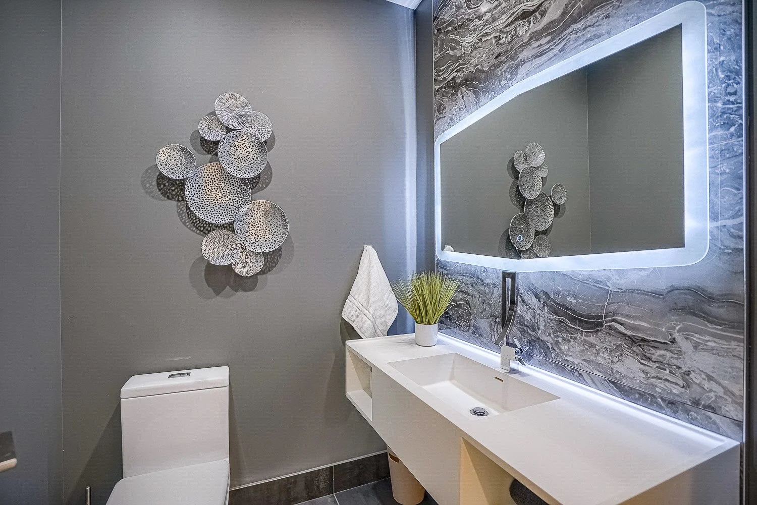 Modern powder room featuring a floating vanity, illuminated LED mirror, and elegant marble-look accent wall with sleek contemporary finishes.