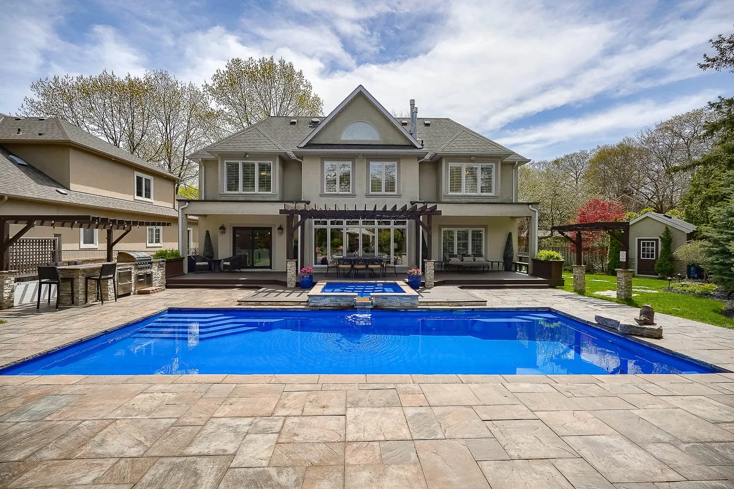 Luxury backyard oasis featuring a resort-style in-ground swimming pool, raised spa, expansive stone patio, covered outdoor entertaining areas, and beautifully landscaped grounds perfect for summer gatherings.