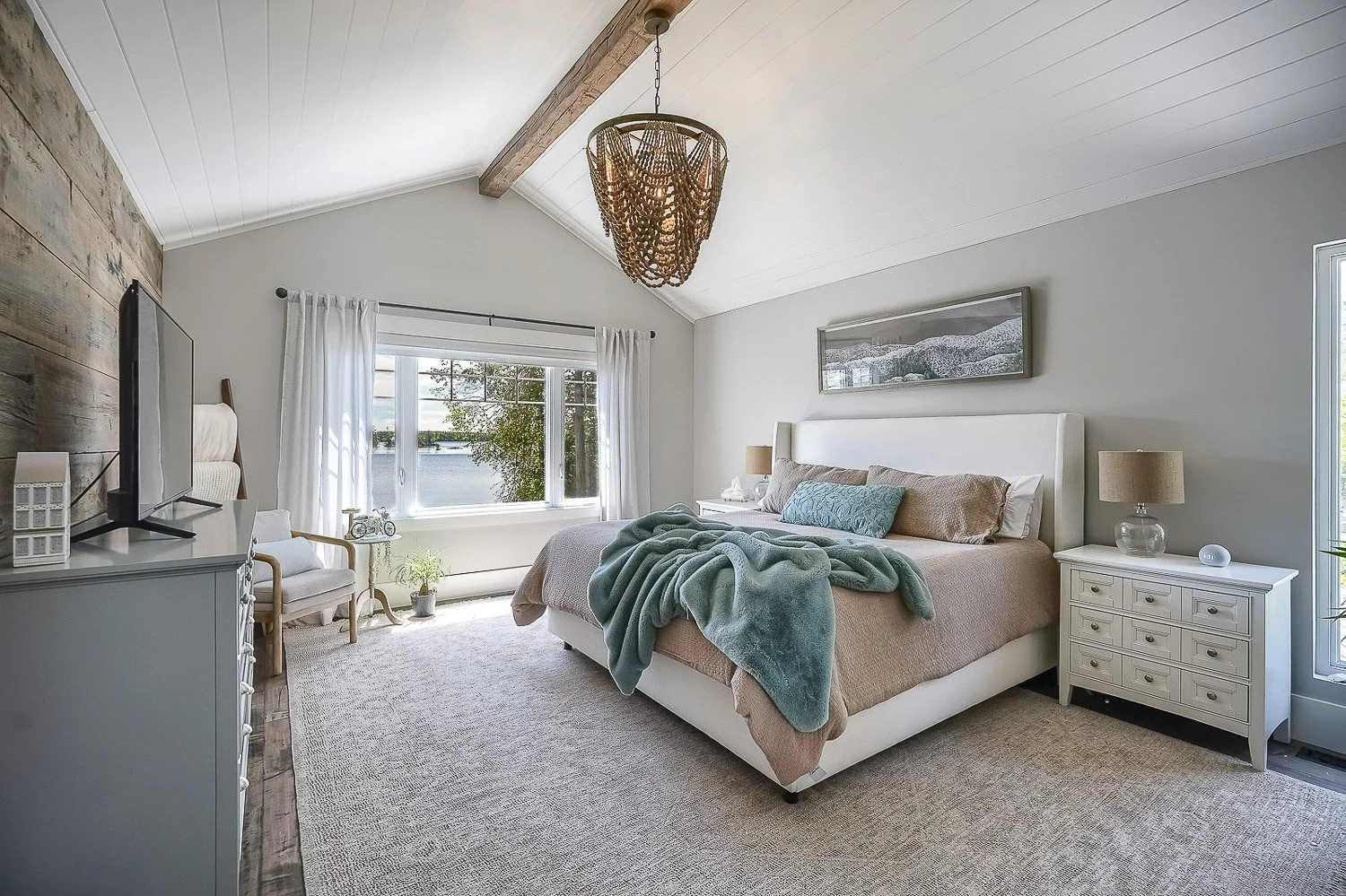 Serene primary bedroom with vaulted ceilings, soft neutral finishes, and tranquil waterfront views, creating a bright and relaxing retreat filled with natural light.