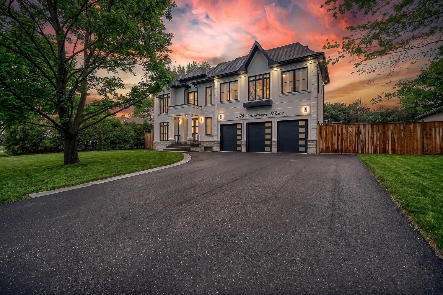 Luxury custom home with triple garage, expansive driveway and dramatic twilight sky
