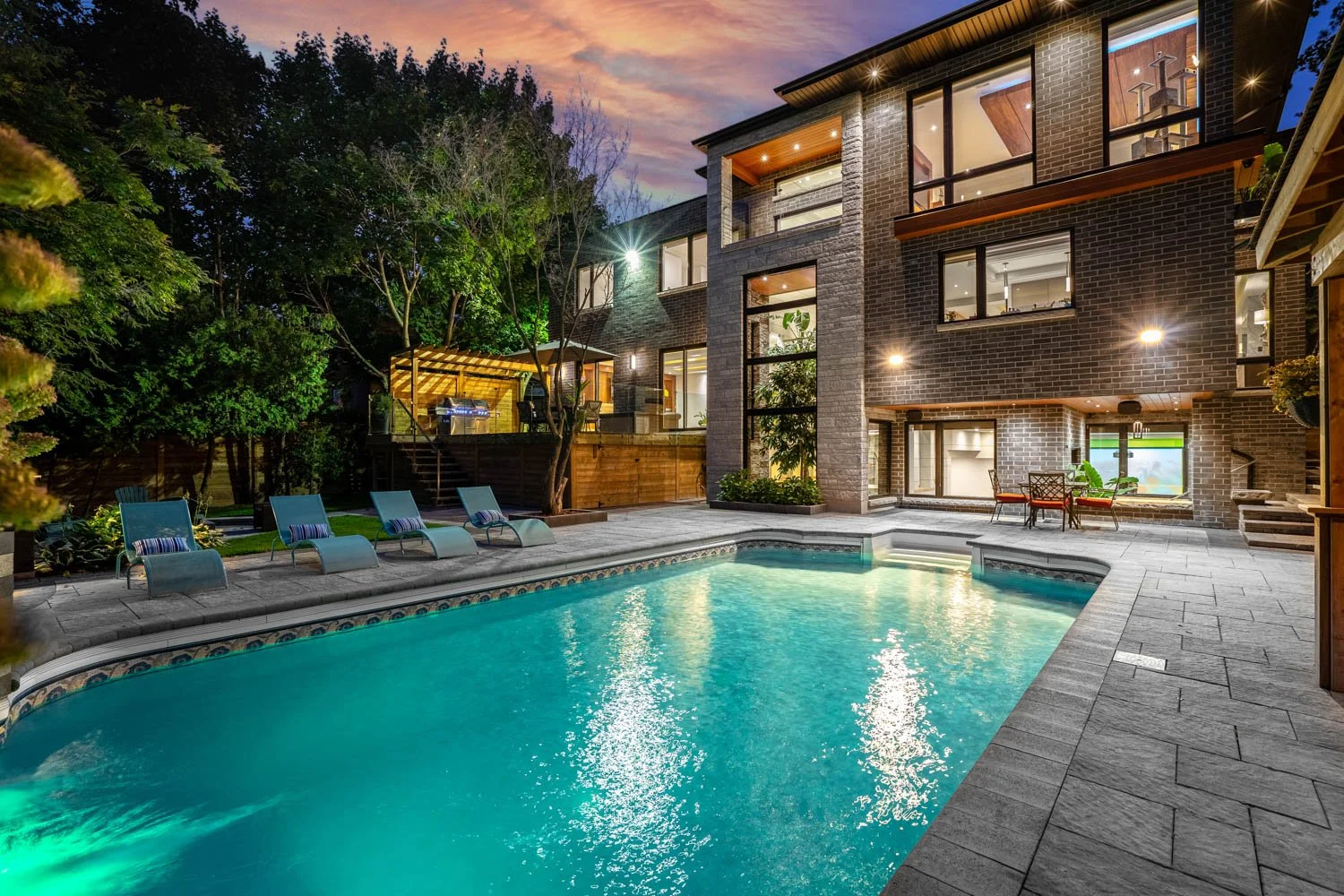 Luxury backyard with illuminated swimming pool, modern custom home and outdoor living space at twilight