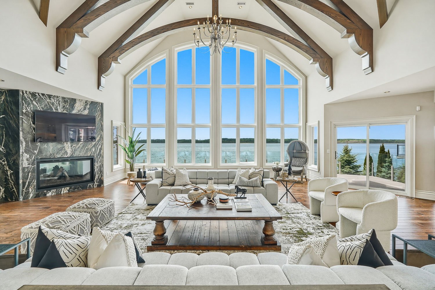 Grand waterfront great room with exposed timber beams, dramatic floor-to-ceiling windows, and breathtaking panoramic lake views, creating an unforgettable luxury living space.