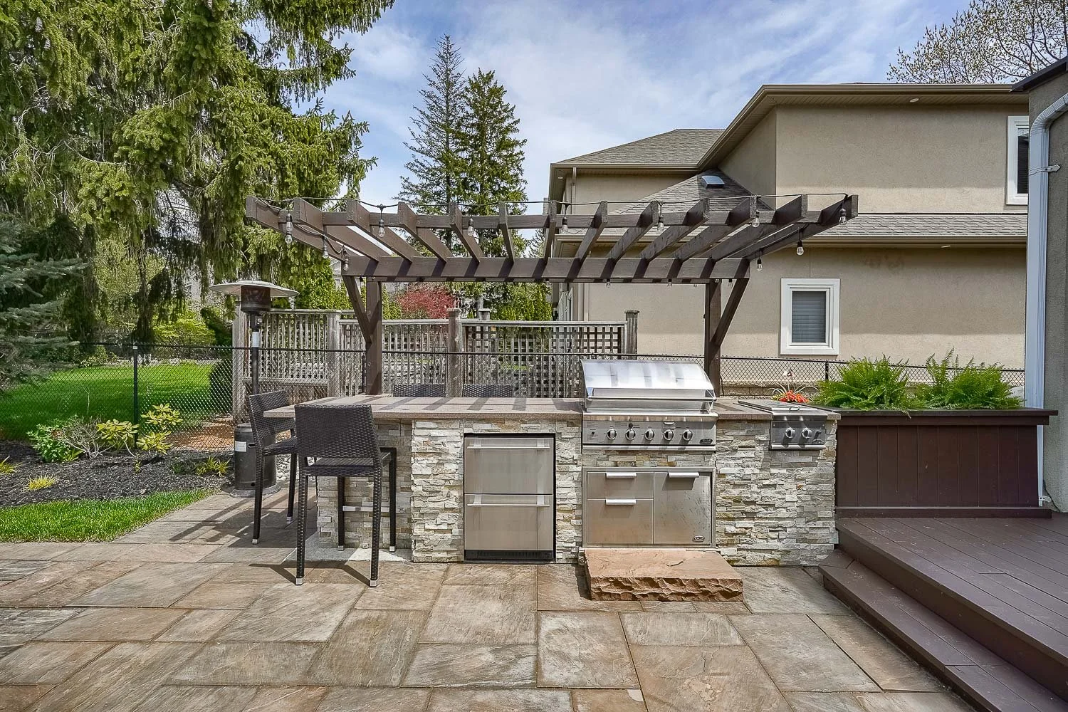 Premium outdoor kitchen with built-in BBQ, stone-clad grilling station, pergola-covered dining area, and spacious patio designed for effortless outdoor entertaining.