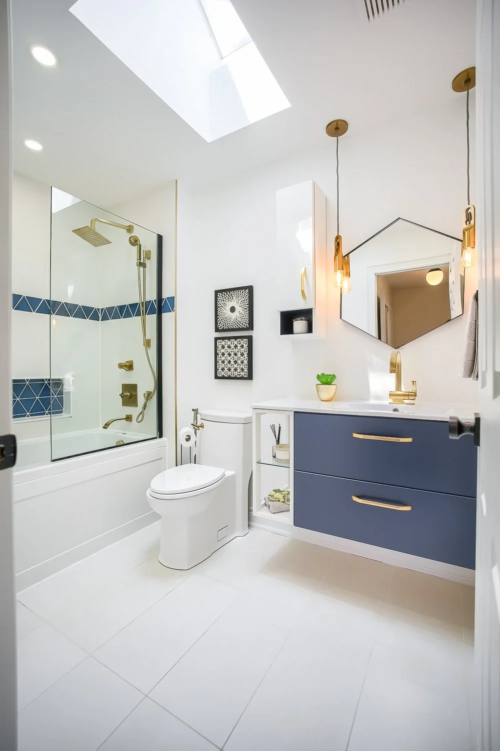 Bright contemporary bathroom with a skylight, custom floating vanity, brass fixtures, and a glass-enclosed tub and shower, combining style with everyday functionality.