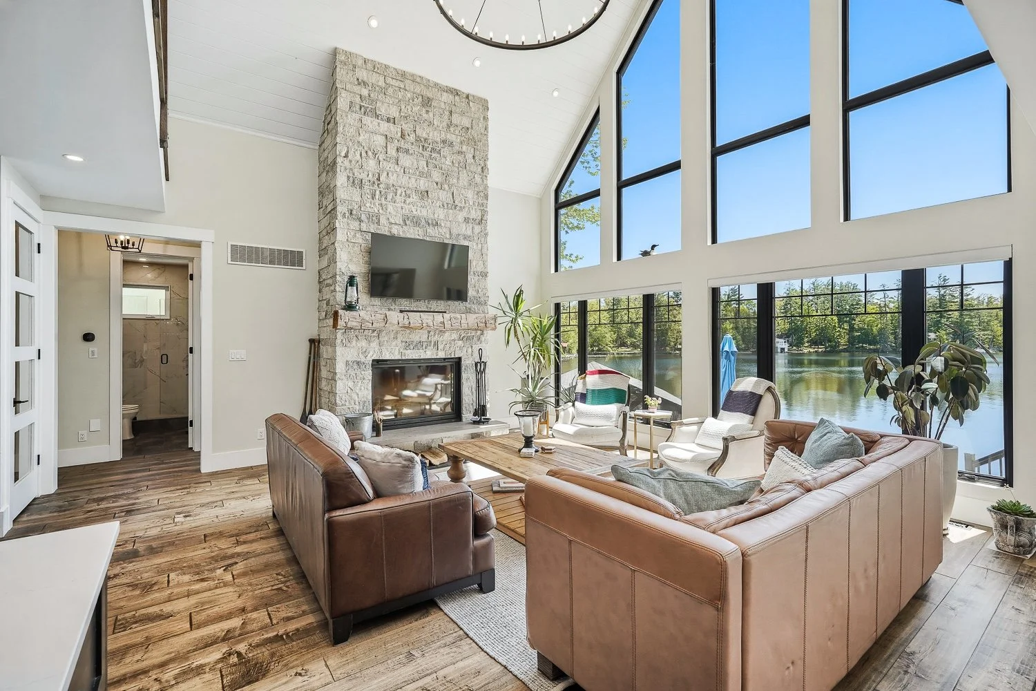Luxury waterfront living room with vaulted ceilings, floor-to-ceiling windows, and a stunning stone fireplace overlooking the lake, professionally photographed for a Toronto real estate listing.
