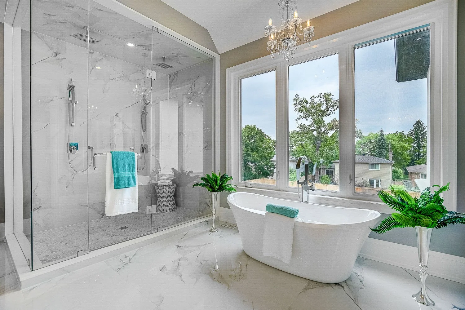 Spa-inspired primary bathroom featuring a freestanding soaking tub, oversized glass walk-in shower, elegant marble finishes, and expansive windows that fill the space with natural light.