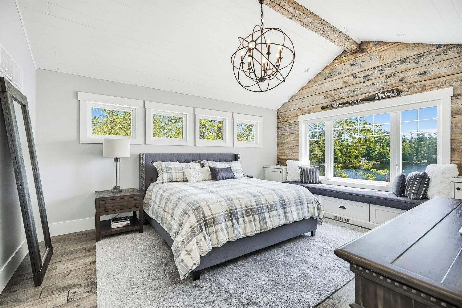 Peaceful primary bedroom with vaulted ceilings, rustic wood accents, and a built-in window seat overlooking the lake, offering a relaxing retreat filled with natural light