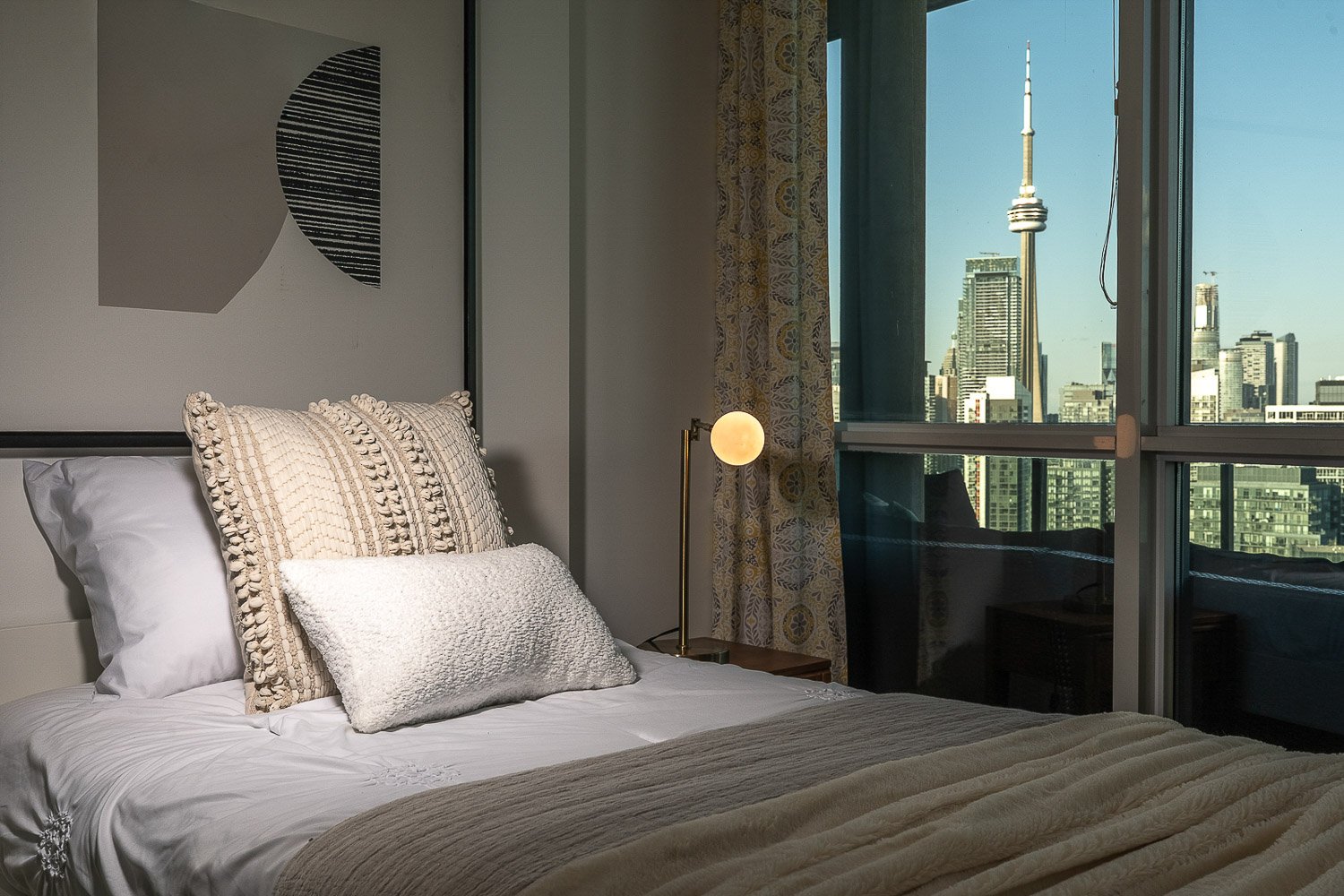 Modern condo bedroom with CN Tower view through floor-to-ceiling windows in downtown Toronto