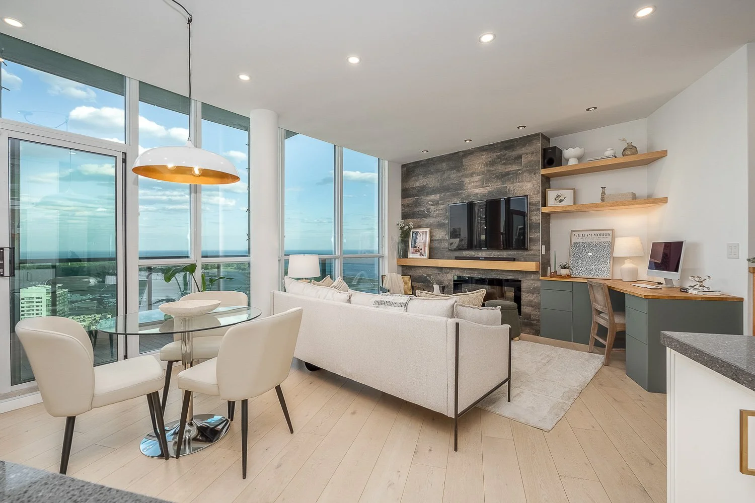 Elegant condo living space with floor-to-ceiling windows, panoramic skyline views, a custom media wall, and a dedicated home office, blending comfort with modern urban design