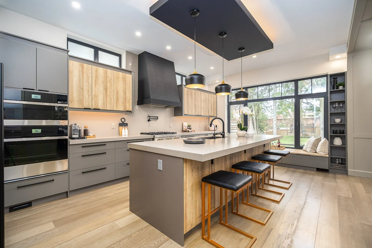 Designer kitchen showcasing a spacious waterfall island, warm wood accents, statement pendant lighting, and a built-in window seat, blending modern style with everyday functionality.