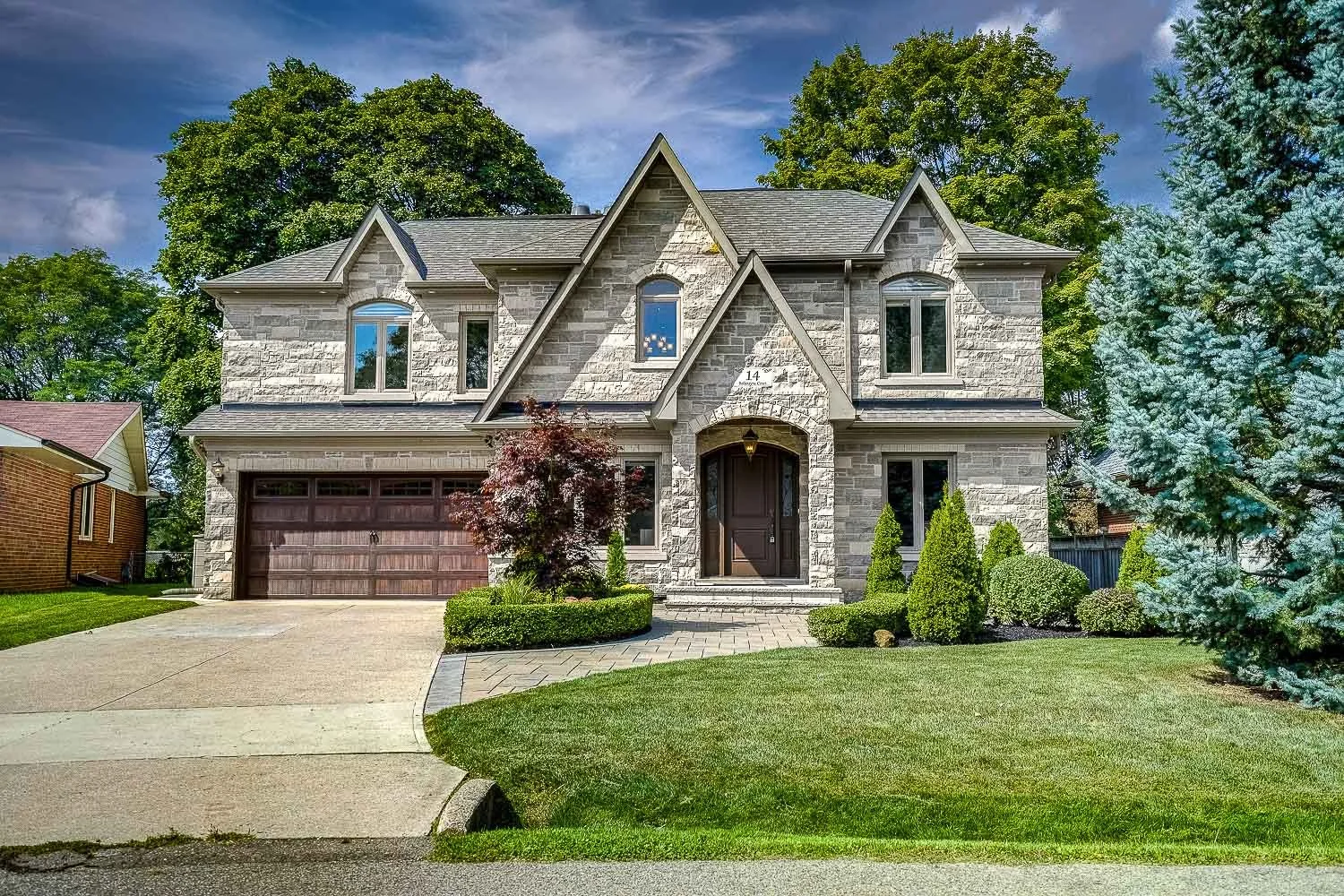 Elegant stone-front luxury home featuring timeless architecture, professionally landscaped gardens, a manicured front lawn, and impressive curb appeal in a prestigious residential setting.