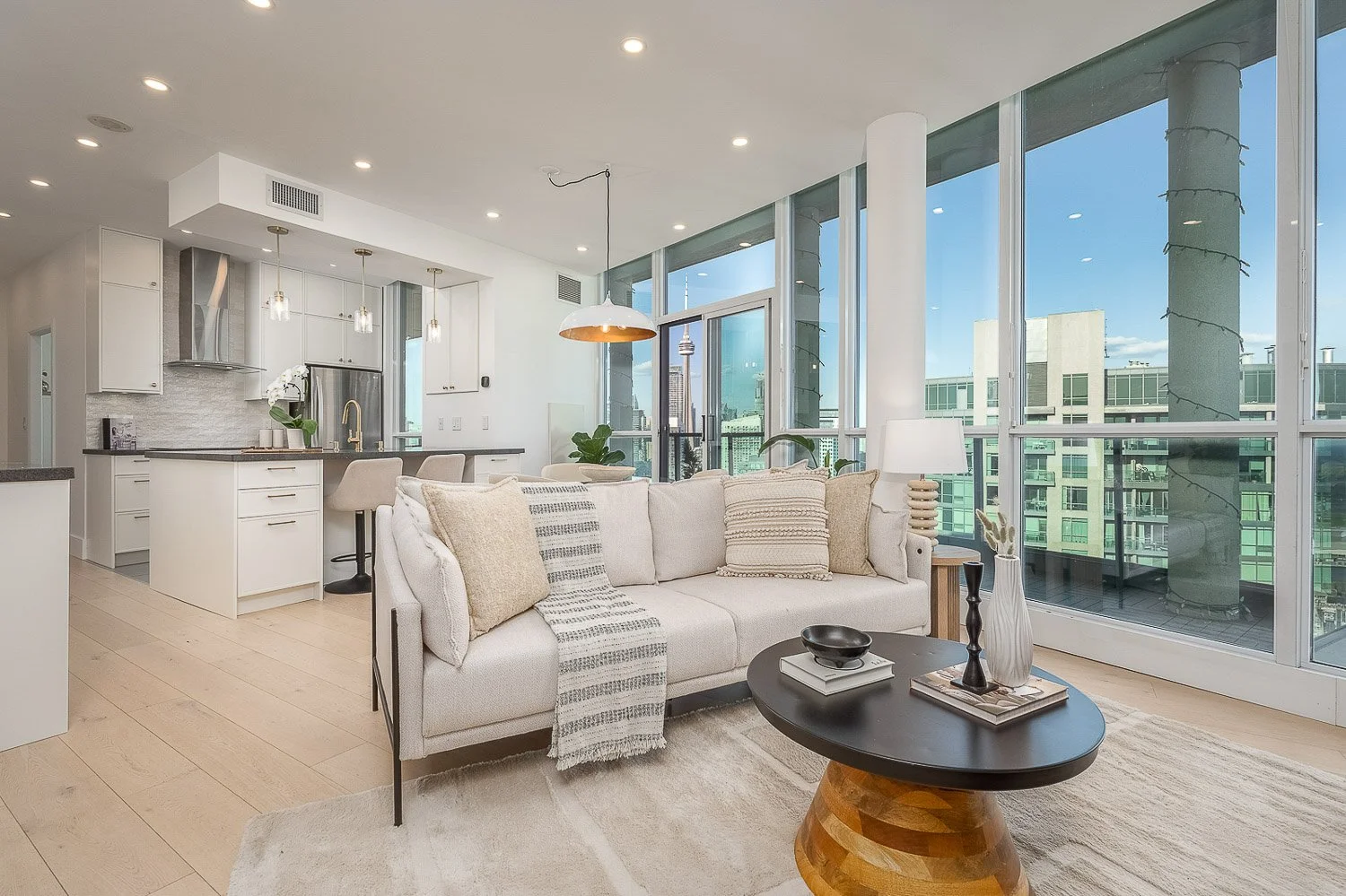 Bright open-concept condo with floor-to-ceiling windows, sweeping city skyline views, and a modern kitchen, creating a light-filled urban living space with seamless indoor-outdoor connection.