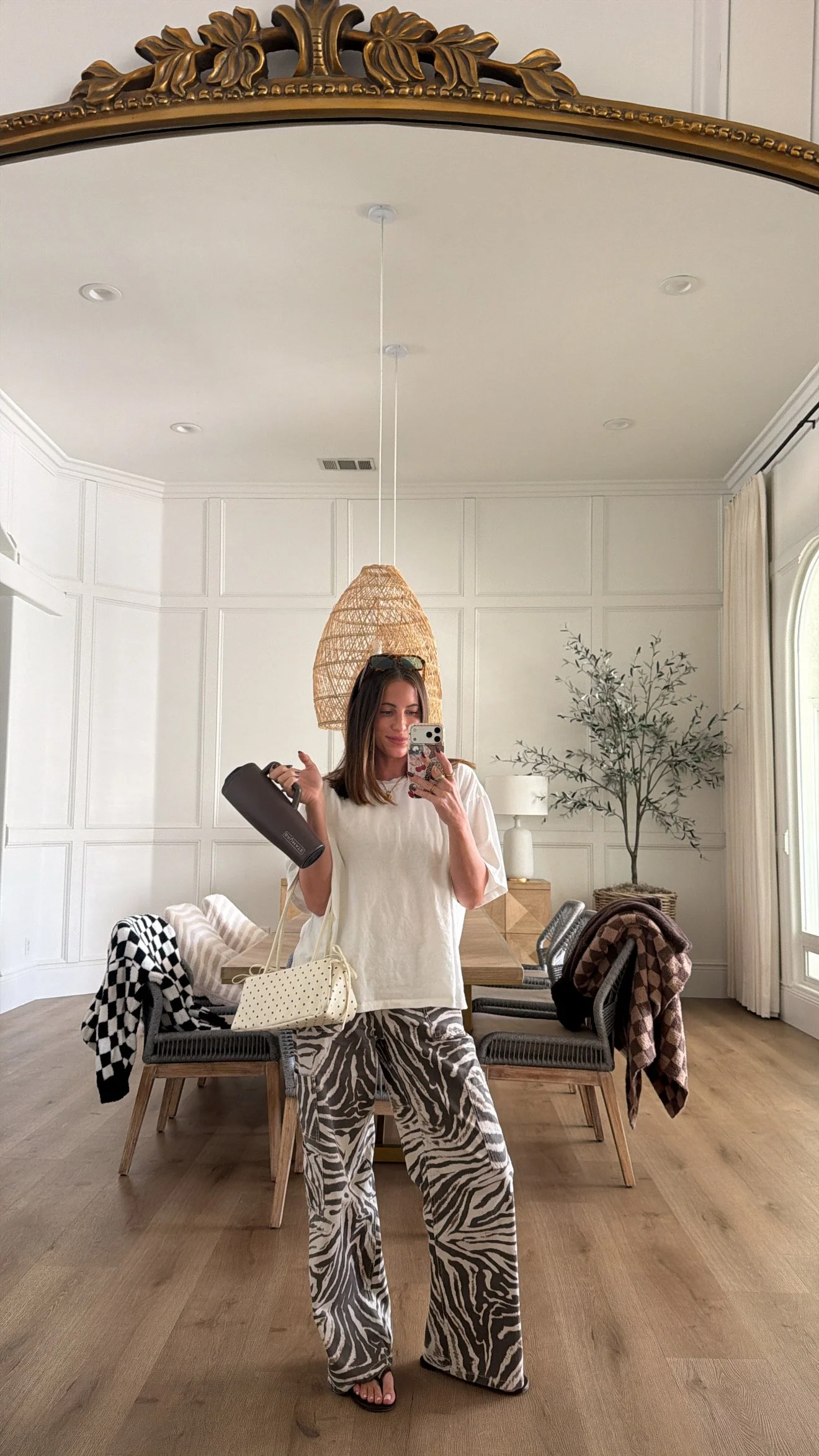 Krista taking a mirror selfie of her outfit, wearing a white oversized shirt, zebra print pants and carrying a polkadot purse.