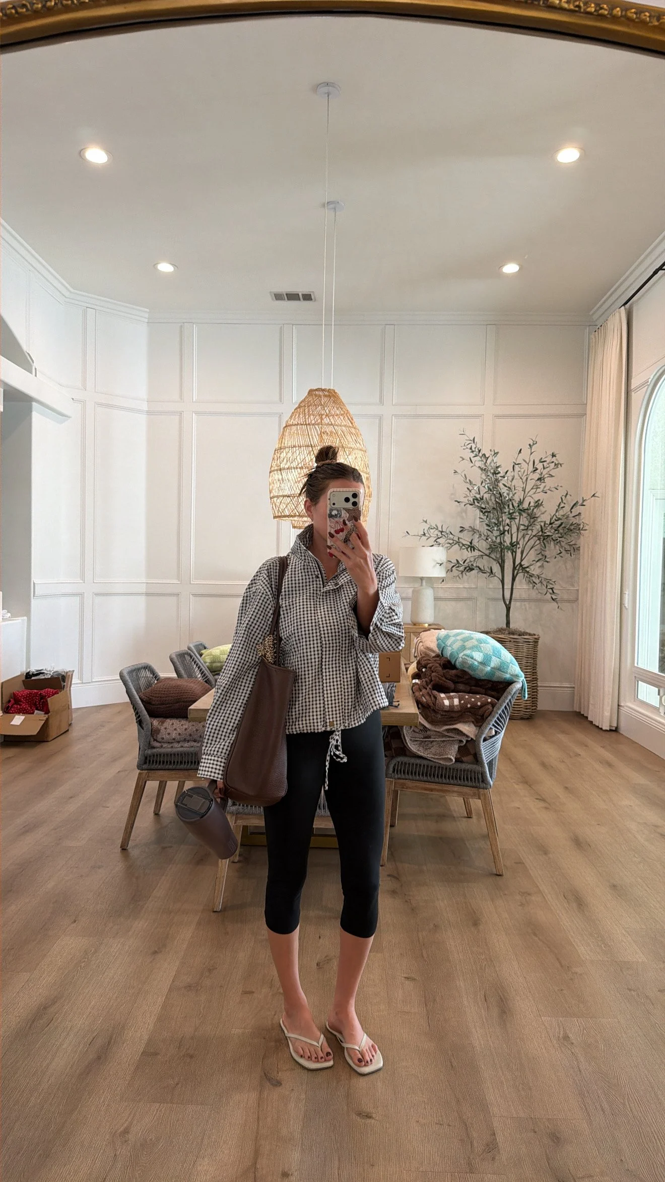 Krista taking a mirror selfie with a gingham jacket on and black capris, white flip flops while carrying her brown insulated brumate and her brown amazon purse.