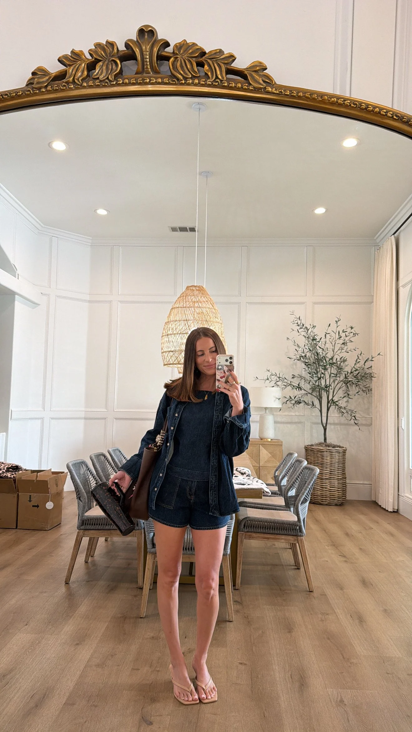 Krista taking a mirror selfie in her home, wearing an all denim outfit while holding a insulated brute cup and nude kitten heel sandals.