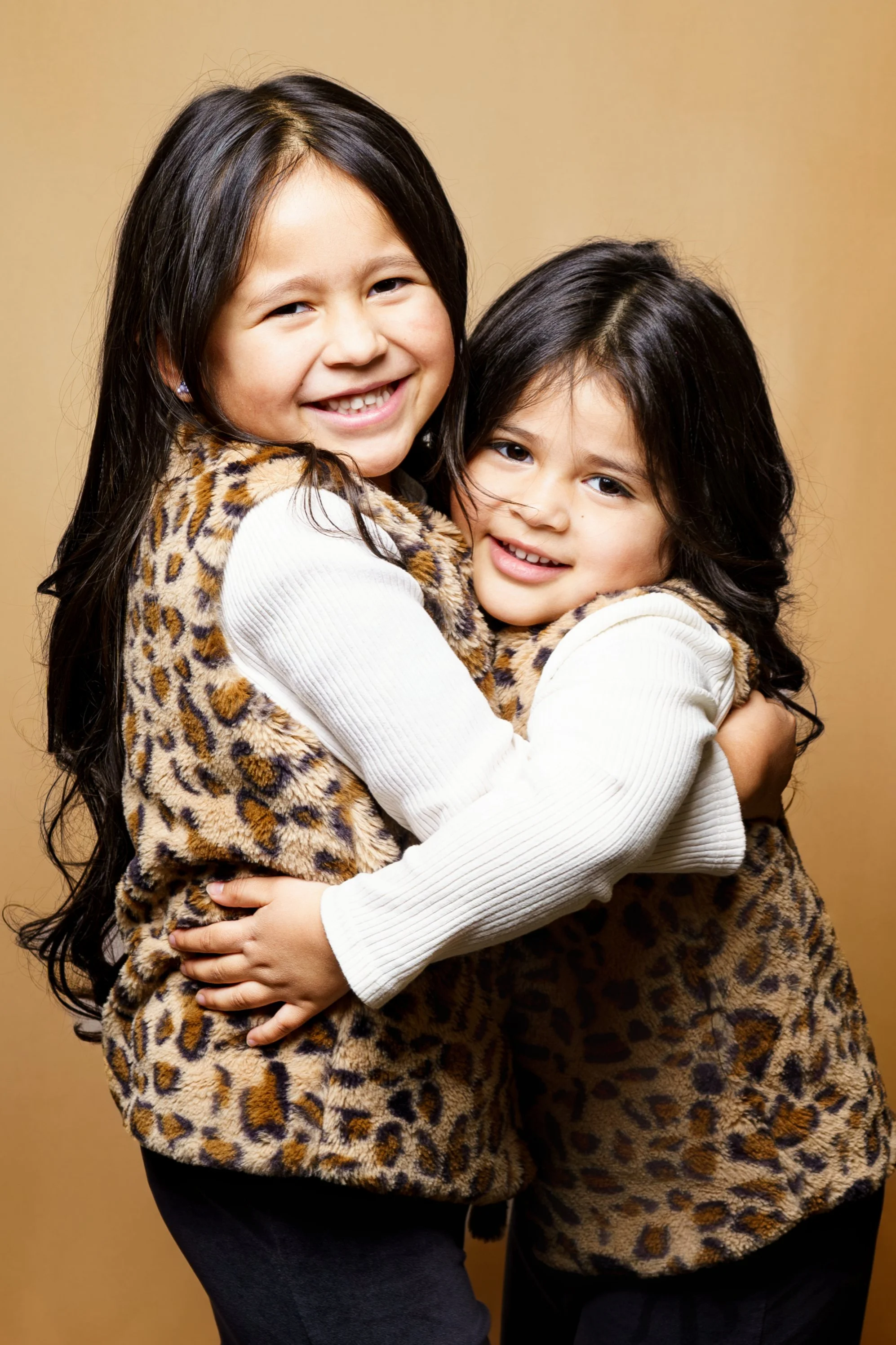 Children and siblings hugging holding  smiling in a finished Picture Day portrait against a warm neutral backdrop