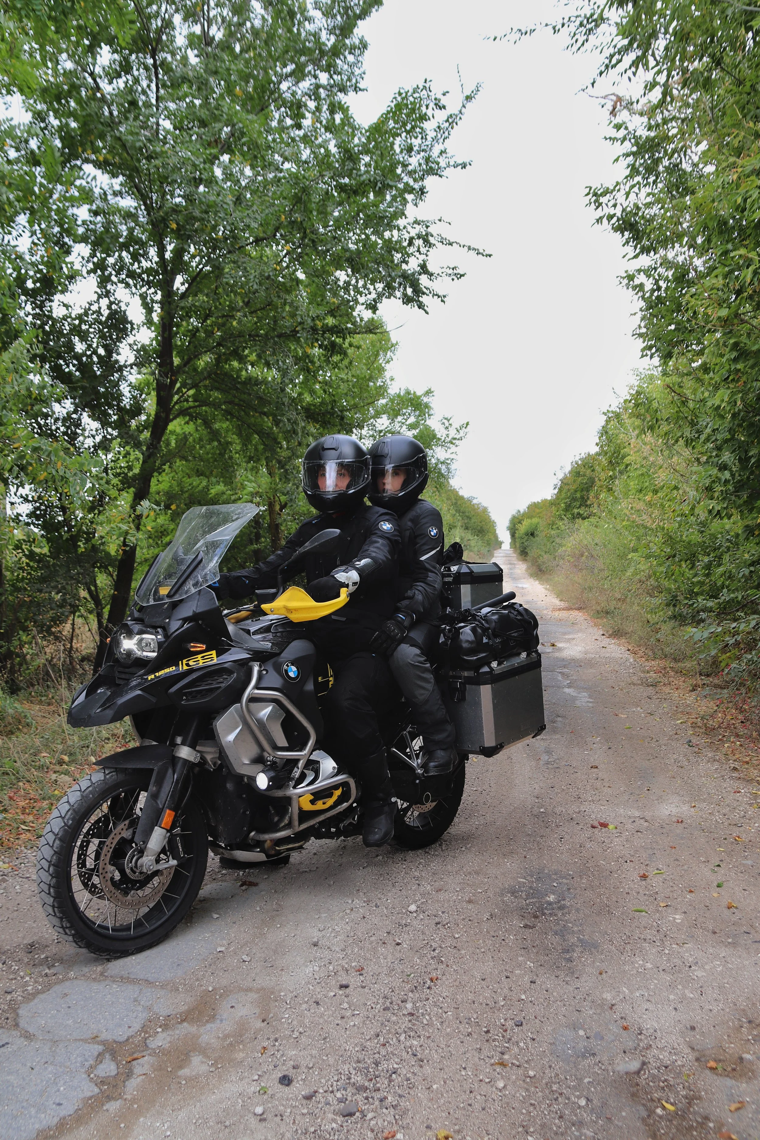 Two motorcyclists in black gear on an adventure motorcycle on a forest trail.