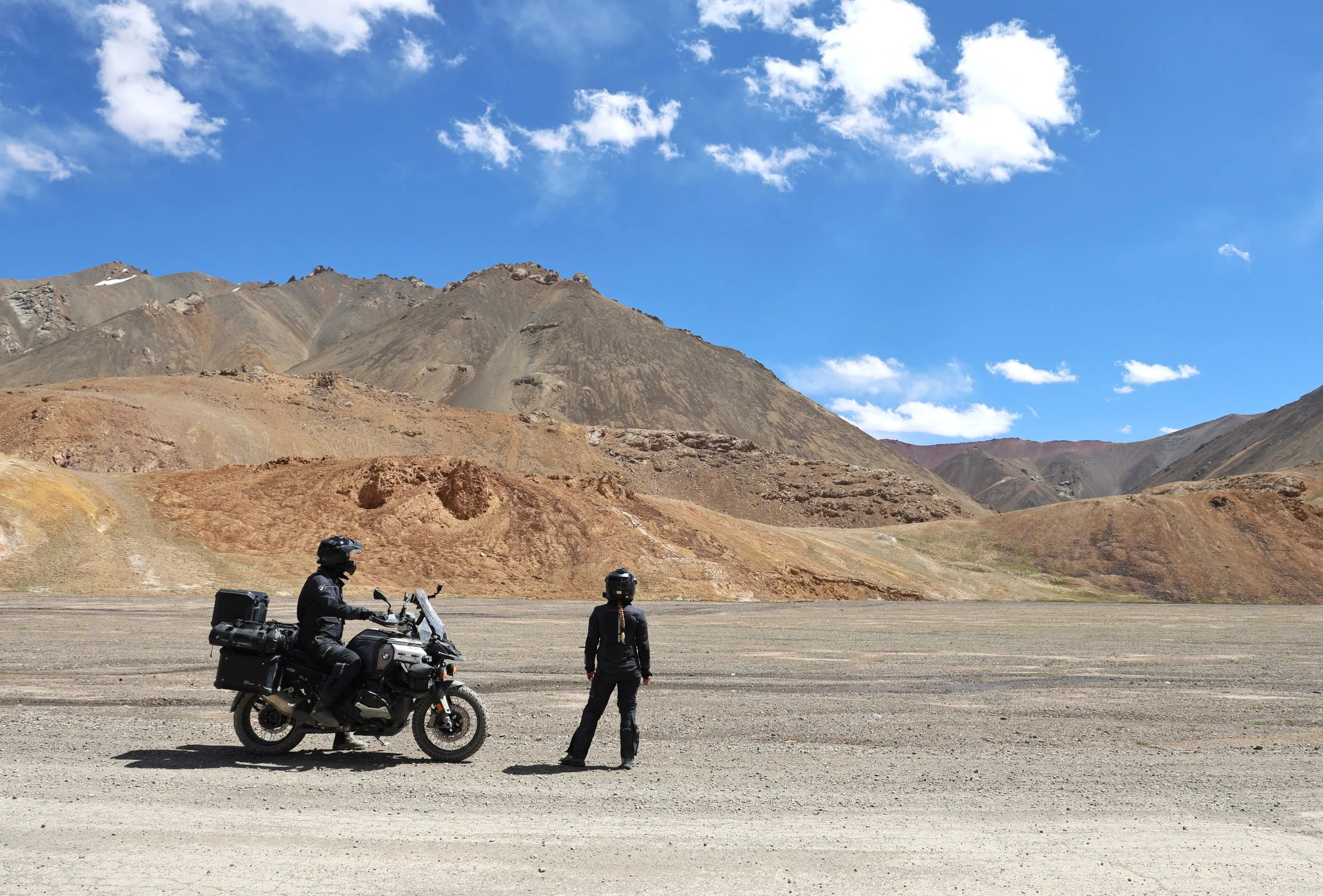 Silhouette of two people with raised arms against a sunset sky, standing in an open field with trees in the background.