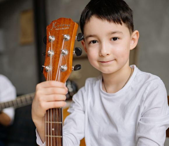 Image of a young person with a guitar in-hand looking to camera