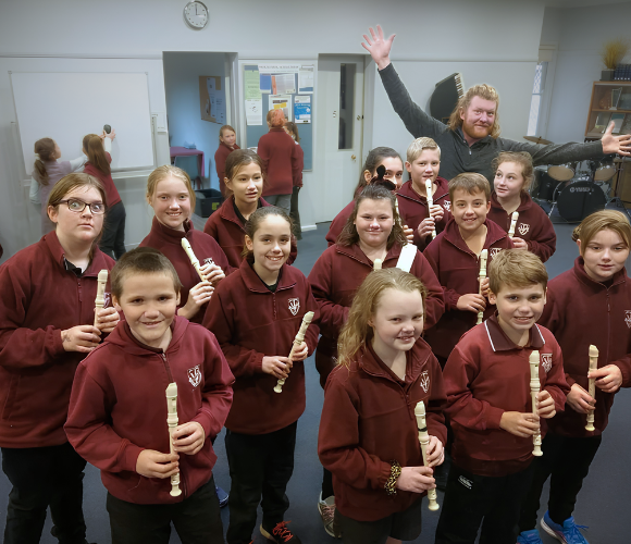 a group of young students looking to camera and smiling the tutor is in the background cheering for the students