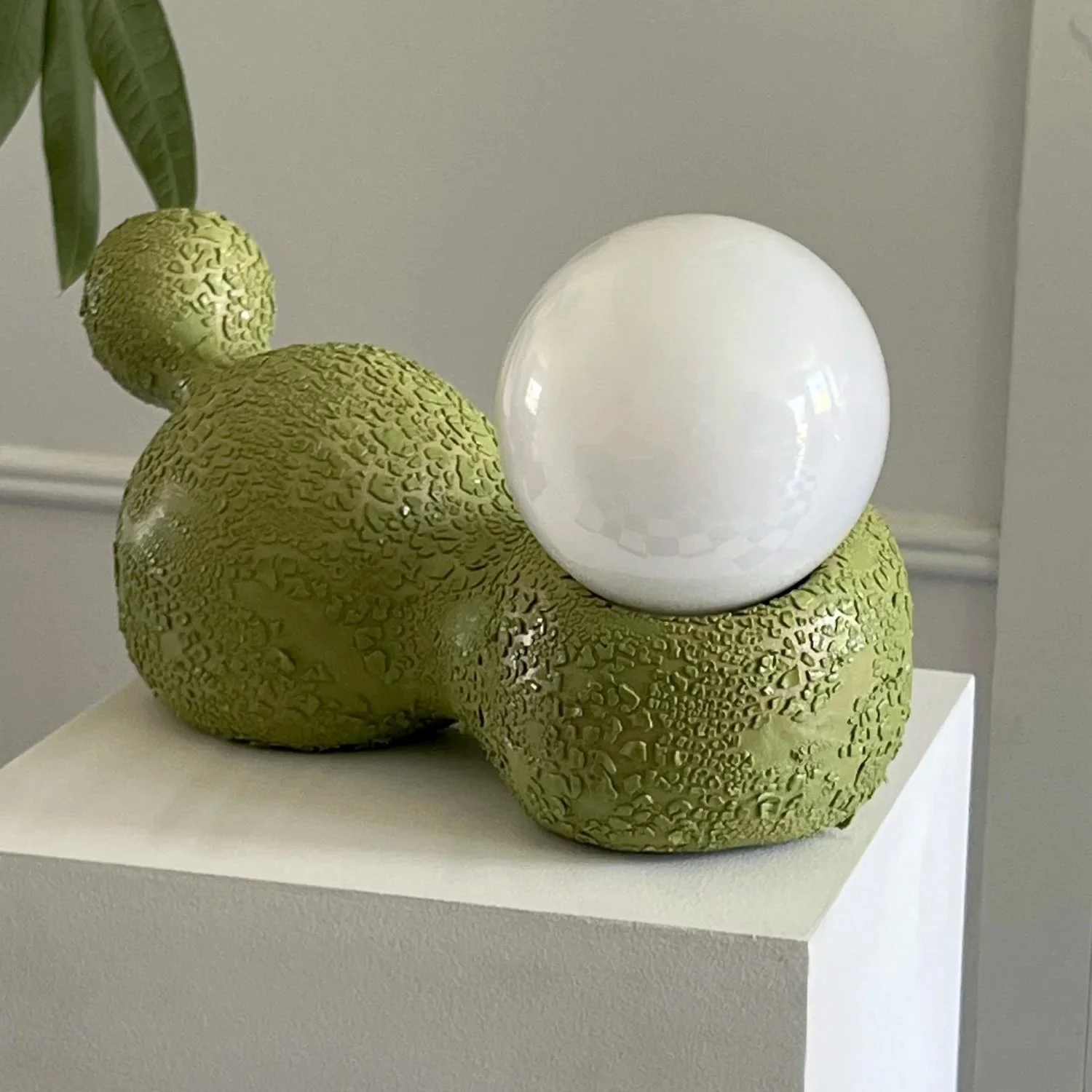 Sculpture of a textured green snake with a large white sphere balanced on its back.