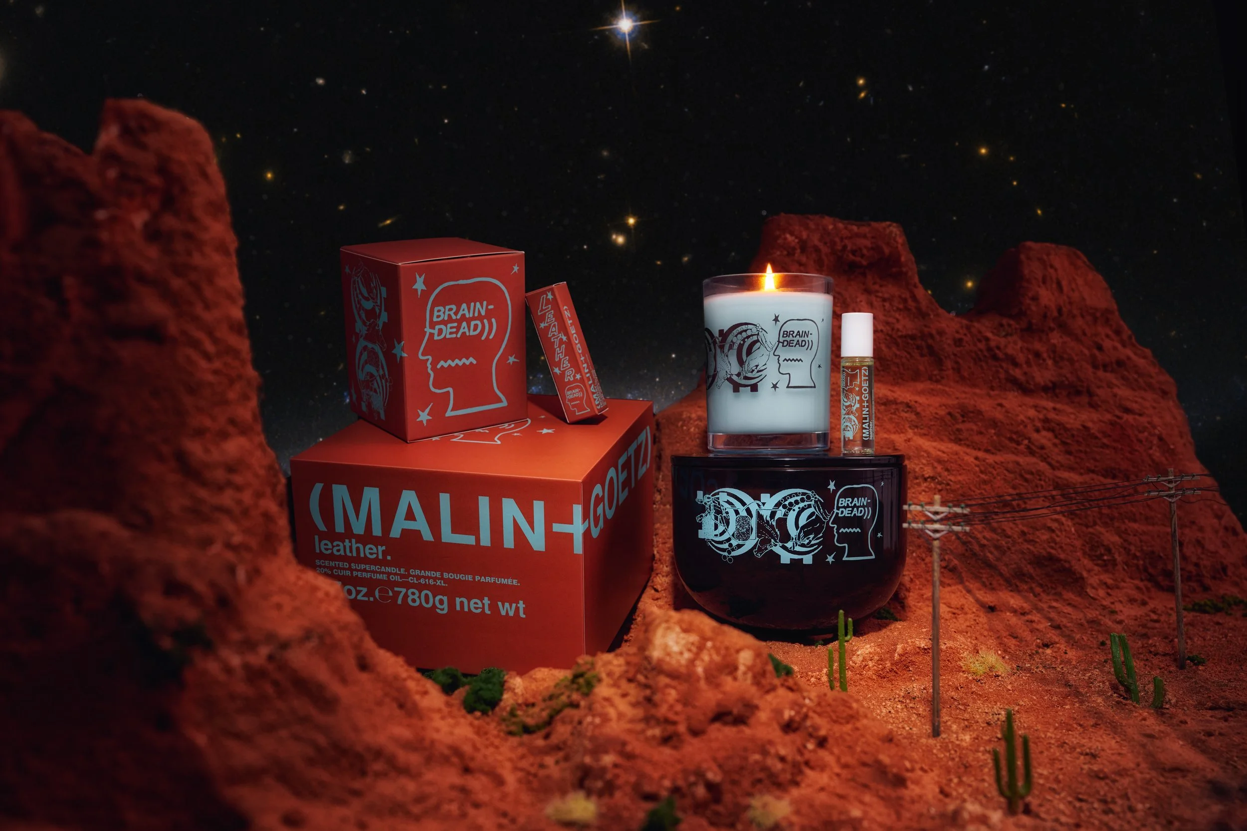 A candle and a perfume bottle with packaging on a rocky, Mars-like landscape with stars in the night sky background.