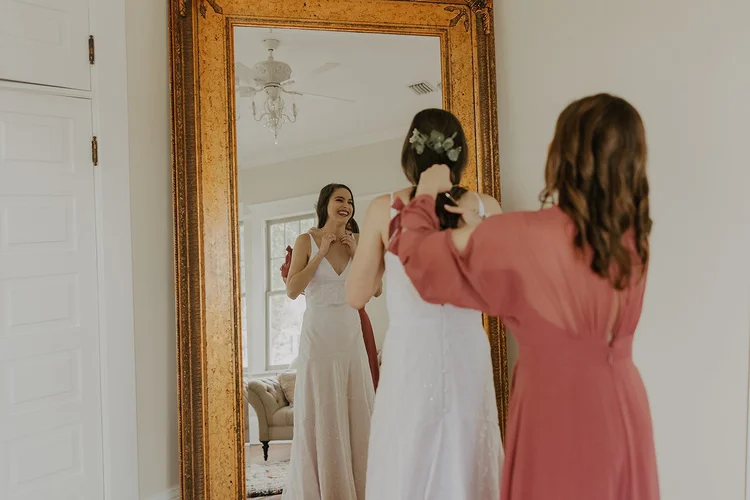 Bridesmaid helping the bride get ready at the mirror