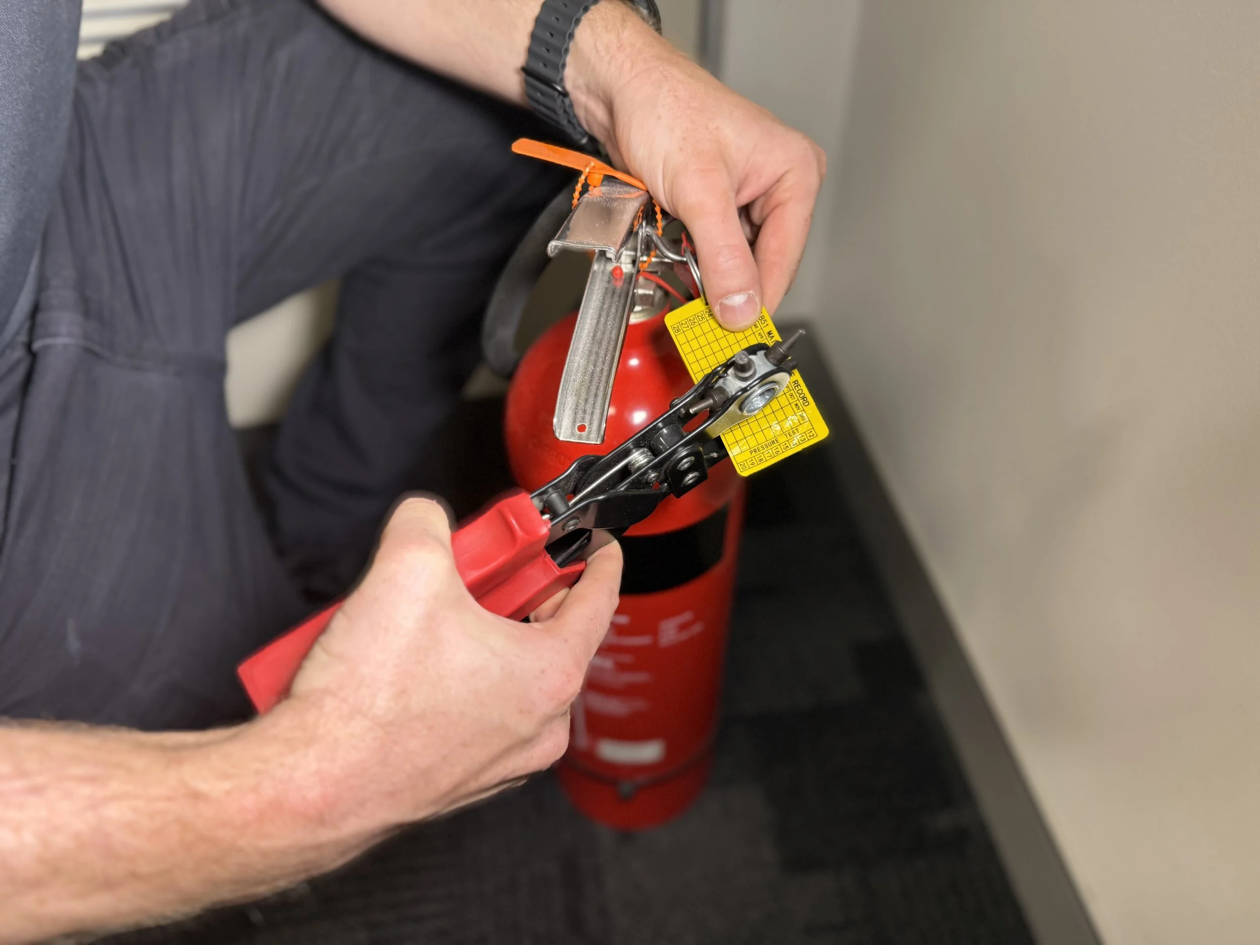 A person using pliers to install or inspect a fire extinguisher with a yellow tag.