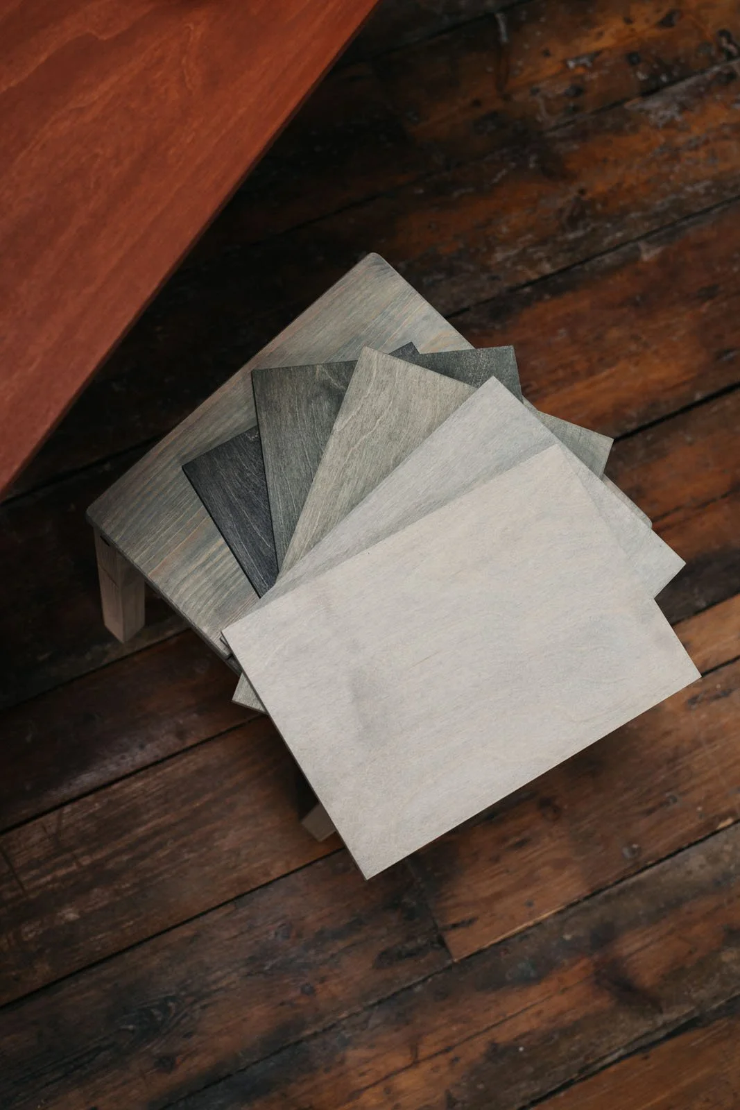 Stained A4 wooden sample boards stacked on a stool.