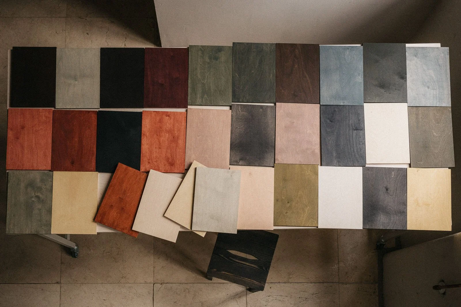 32 stained A4 wooden sample boards layered flat on a table