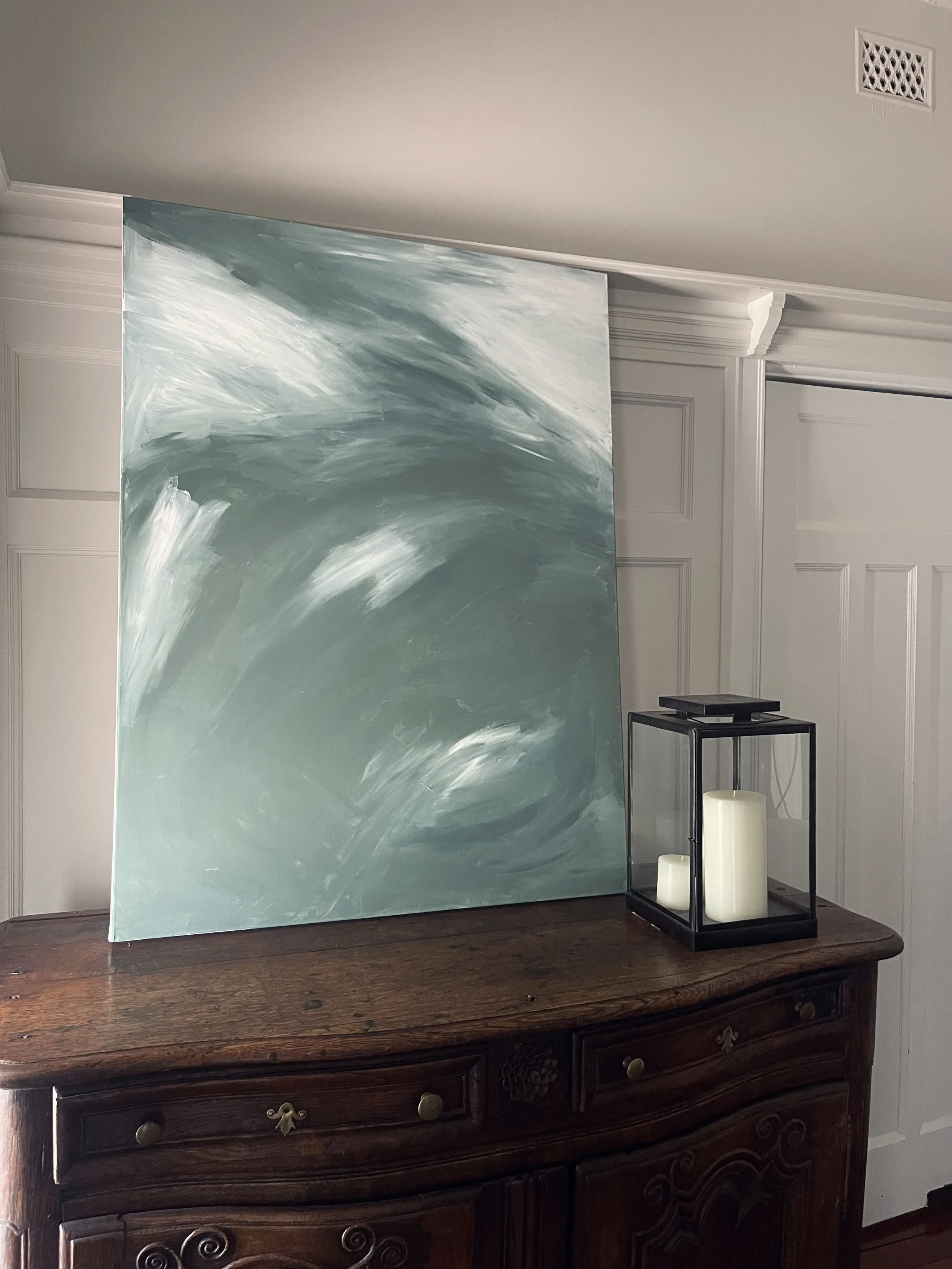 Abstract painting on wooden dresser next to lantern with candles
