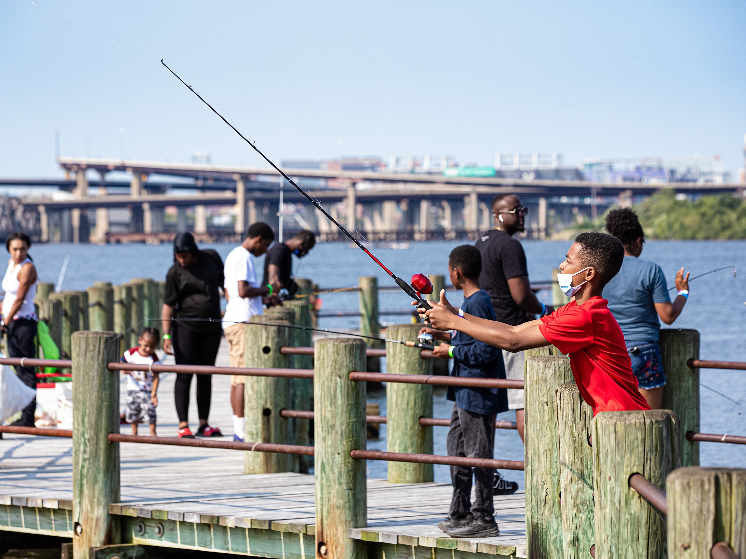  A dozen residents on pier, with boy in foreground using fishing pole 