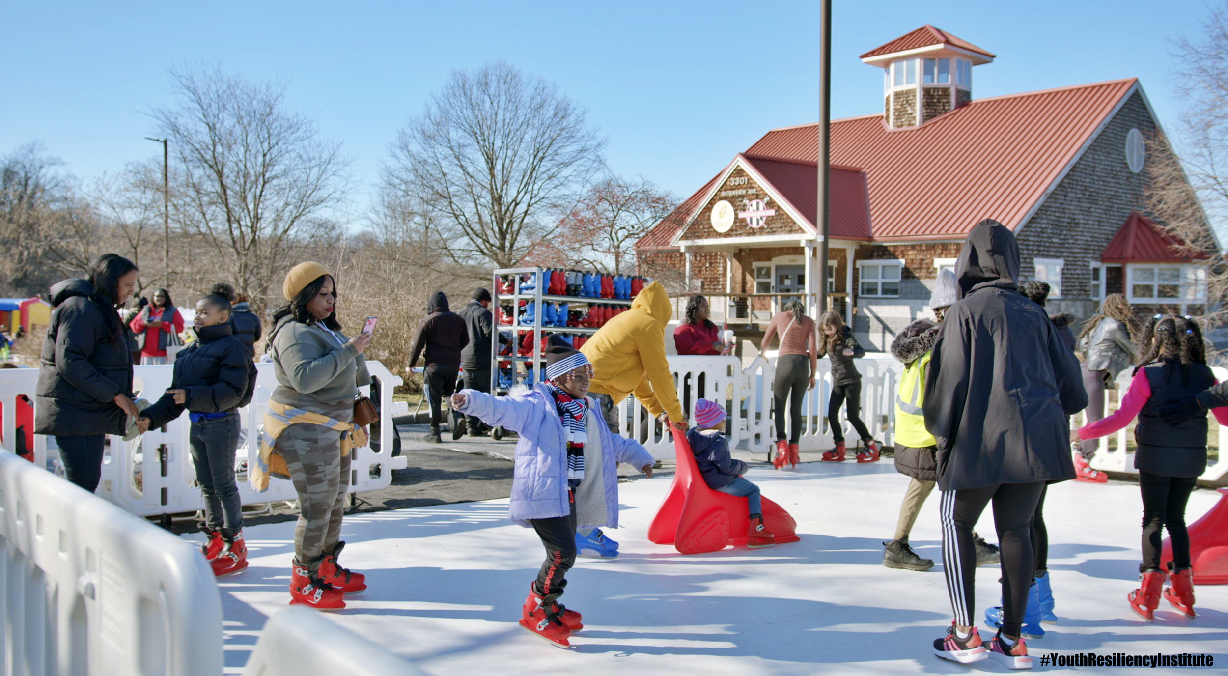  People are enjoying the ice-skating rink in Middle Branch Park with a view of the red roof boathouse in the background. 