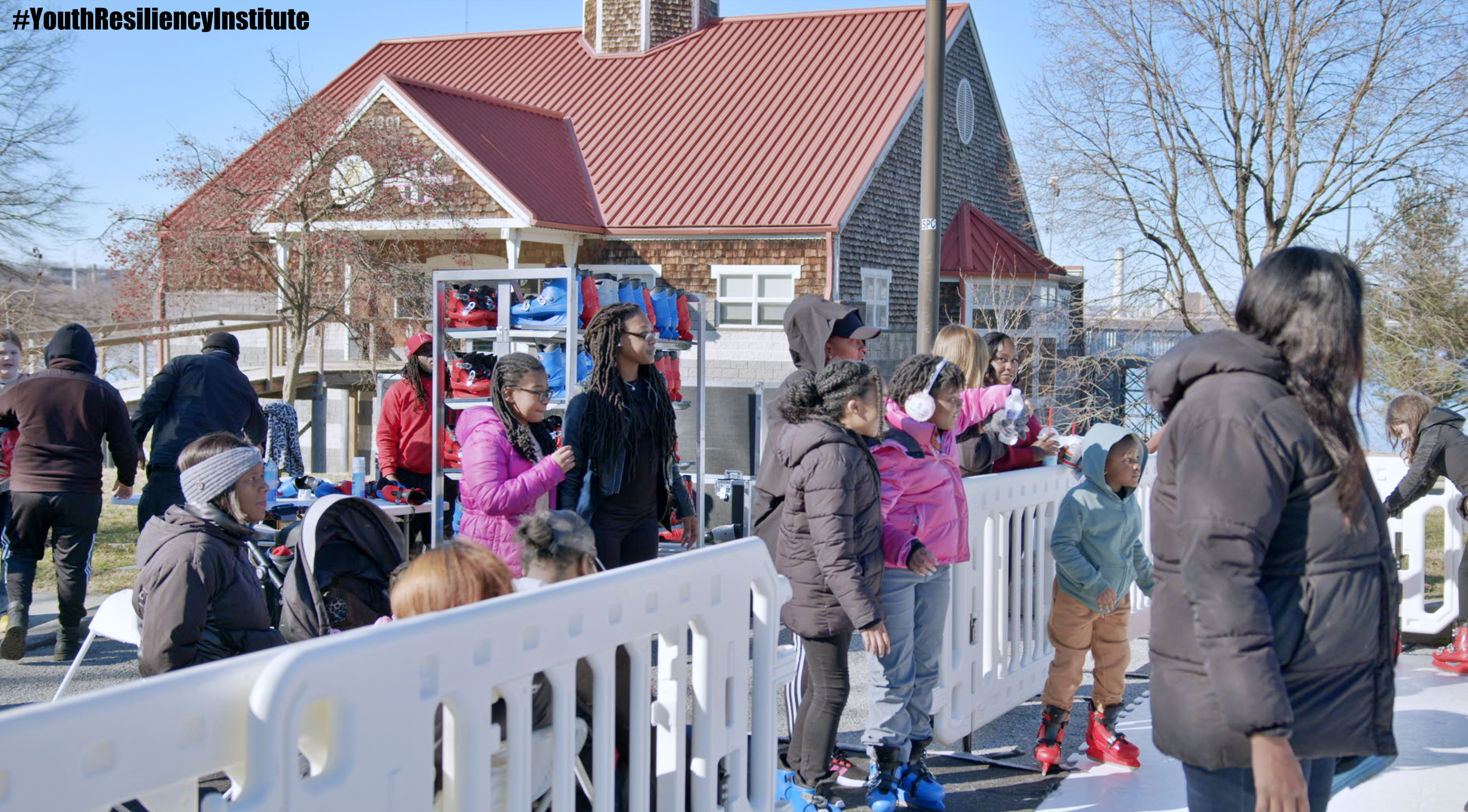  People are enjoying the ice-skating rink in Middle Branch Park with a view of the red roof boathouse in the background. 