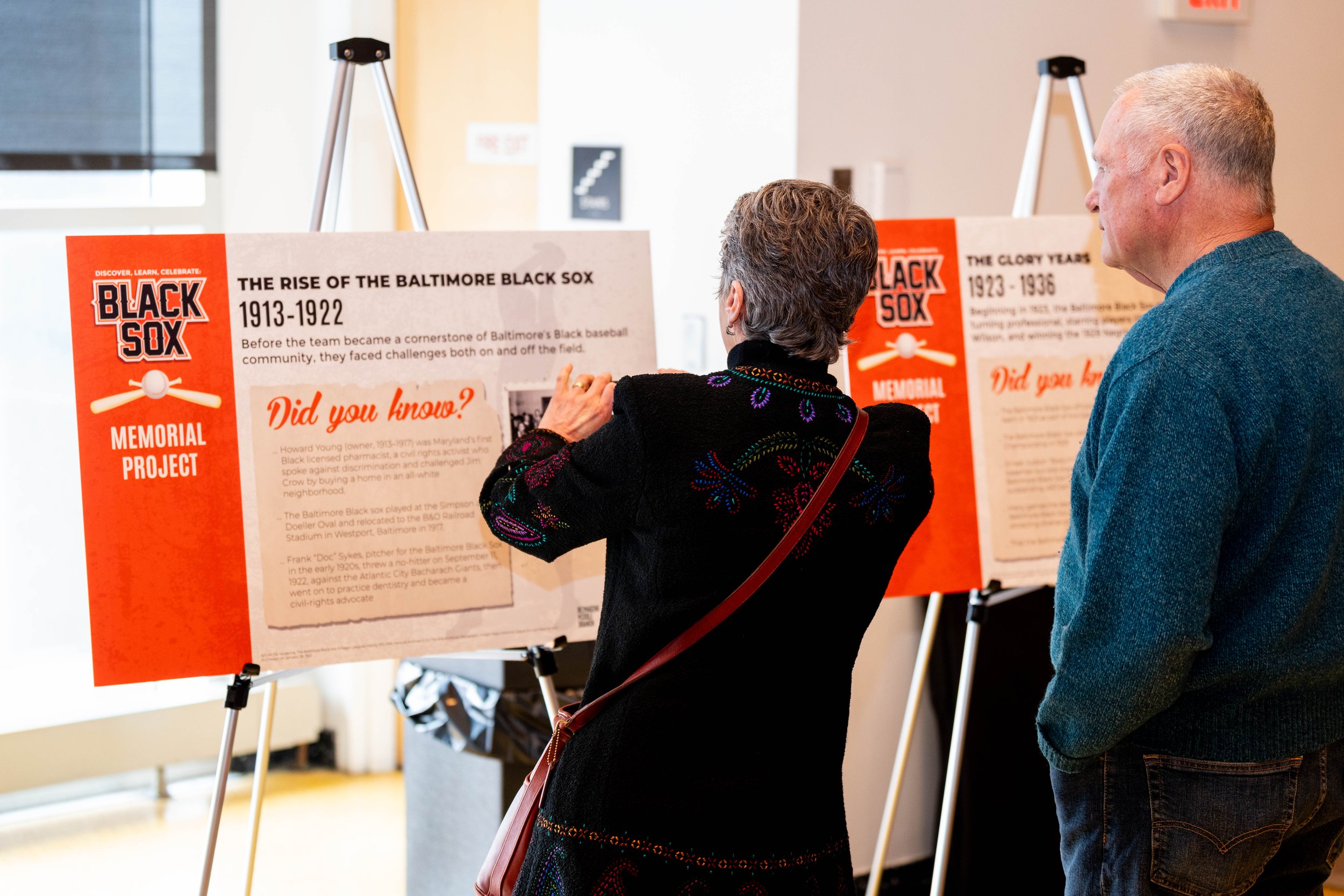  Two people stand looking at a poster featuring historical research about the Baltimore Black Sox. The research was compiled by Coppin State students.  