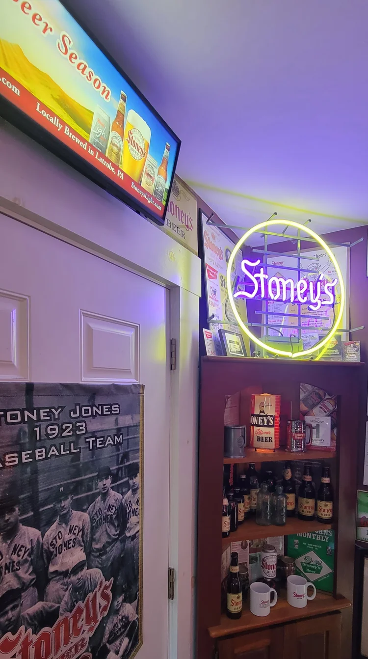 Round Stoney's neon sign beside a TV and stocked shelves
