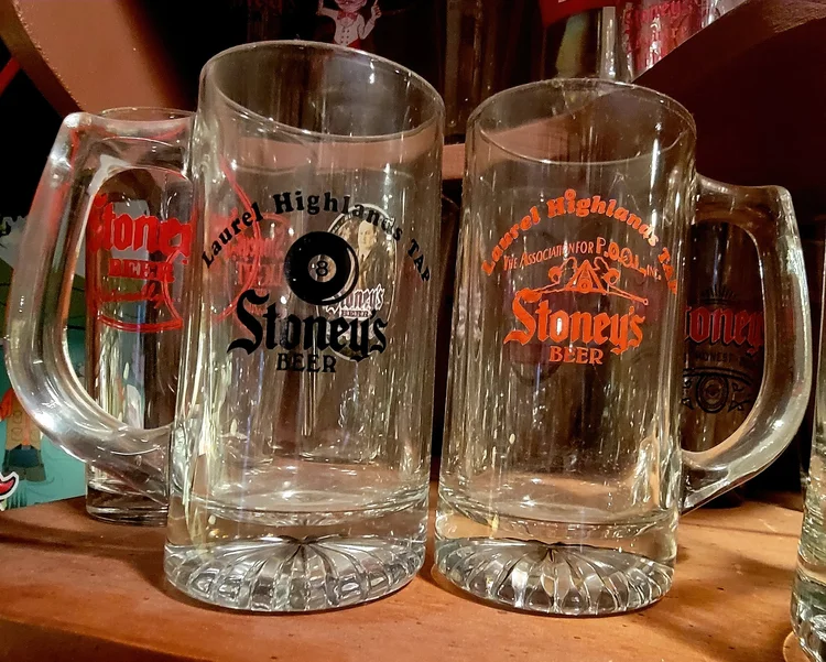 Vintage Stoney's glass mugs in front of advertising