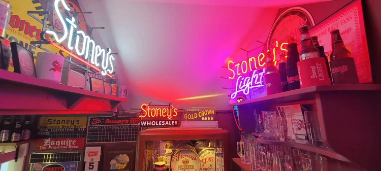 Stoney's Light neon sign over a shelf of cans and advertising