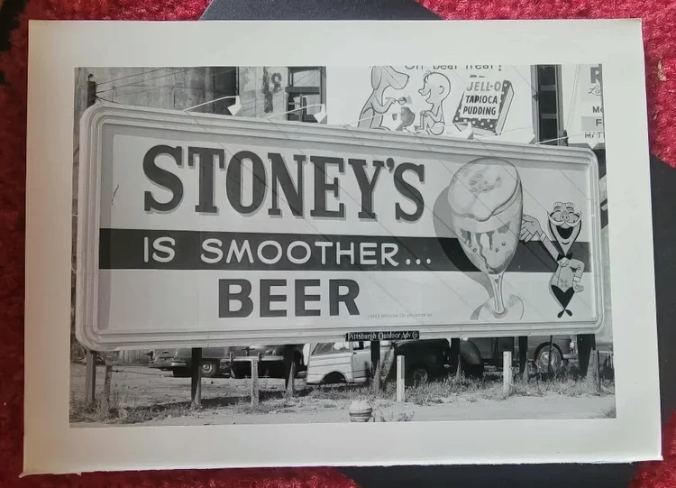 Black-and-white photo of a Stoney's billboard with classic cars
