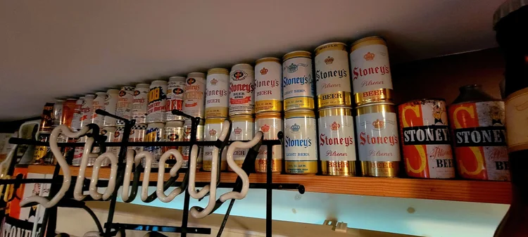 Shelf of vintage Stoney's cans beneath a wooden Stoney's sign